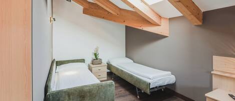 Une petite pièce compacte, dotée de deux lits simples, d’une commode en bois et d’un puits de lumière.