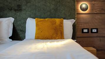 Una cama bien tendida con sábanas blancas y un cojín amarillo mostaza, frente a un cabecero tapizado en verde con un diseño geométrico.