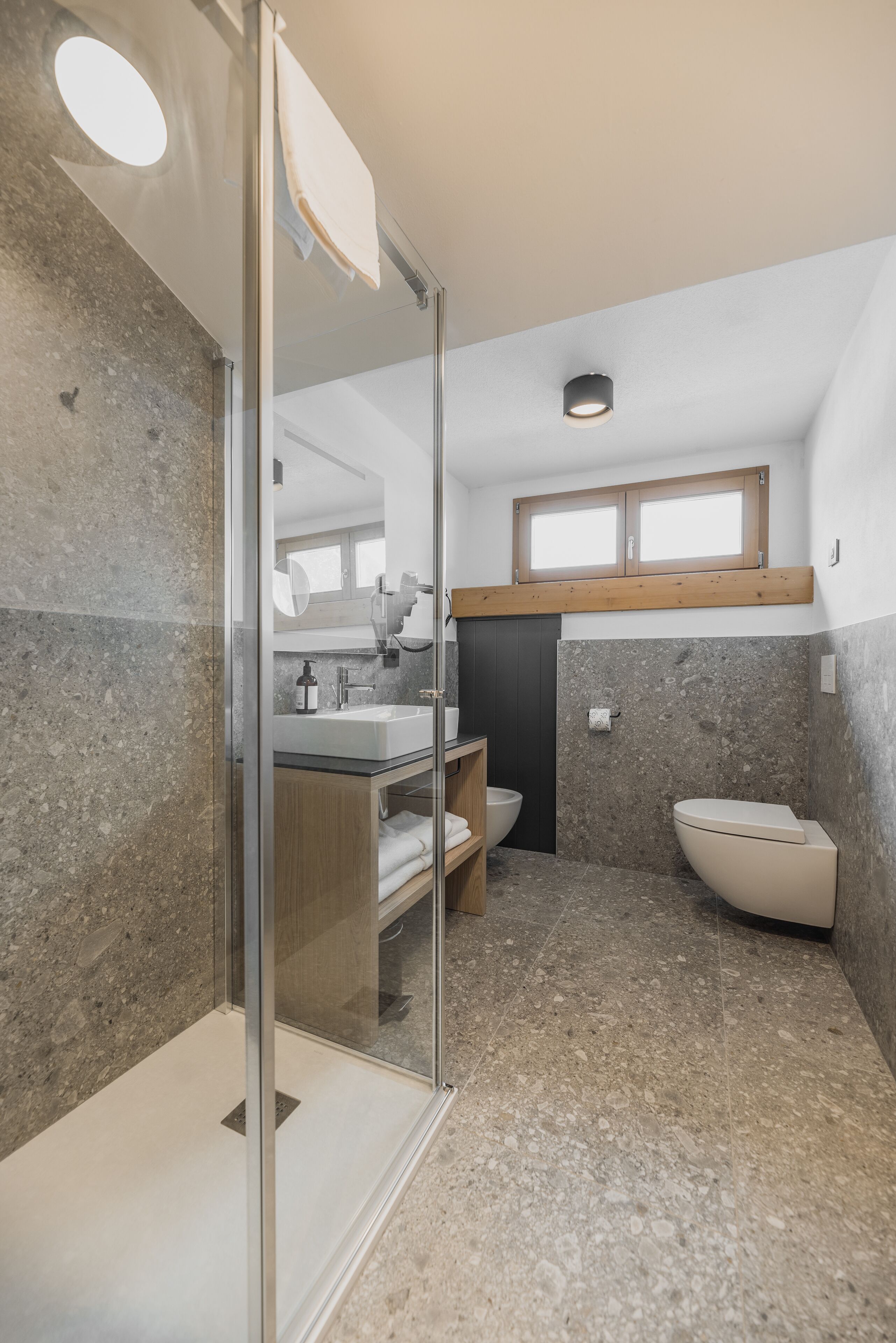 Un bagno moderno con cabina doccia in vetro, mobile bagno in legno, un water e un lavabo.