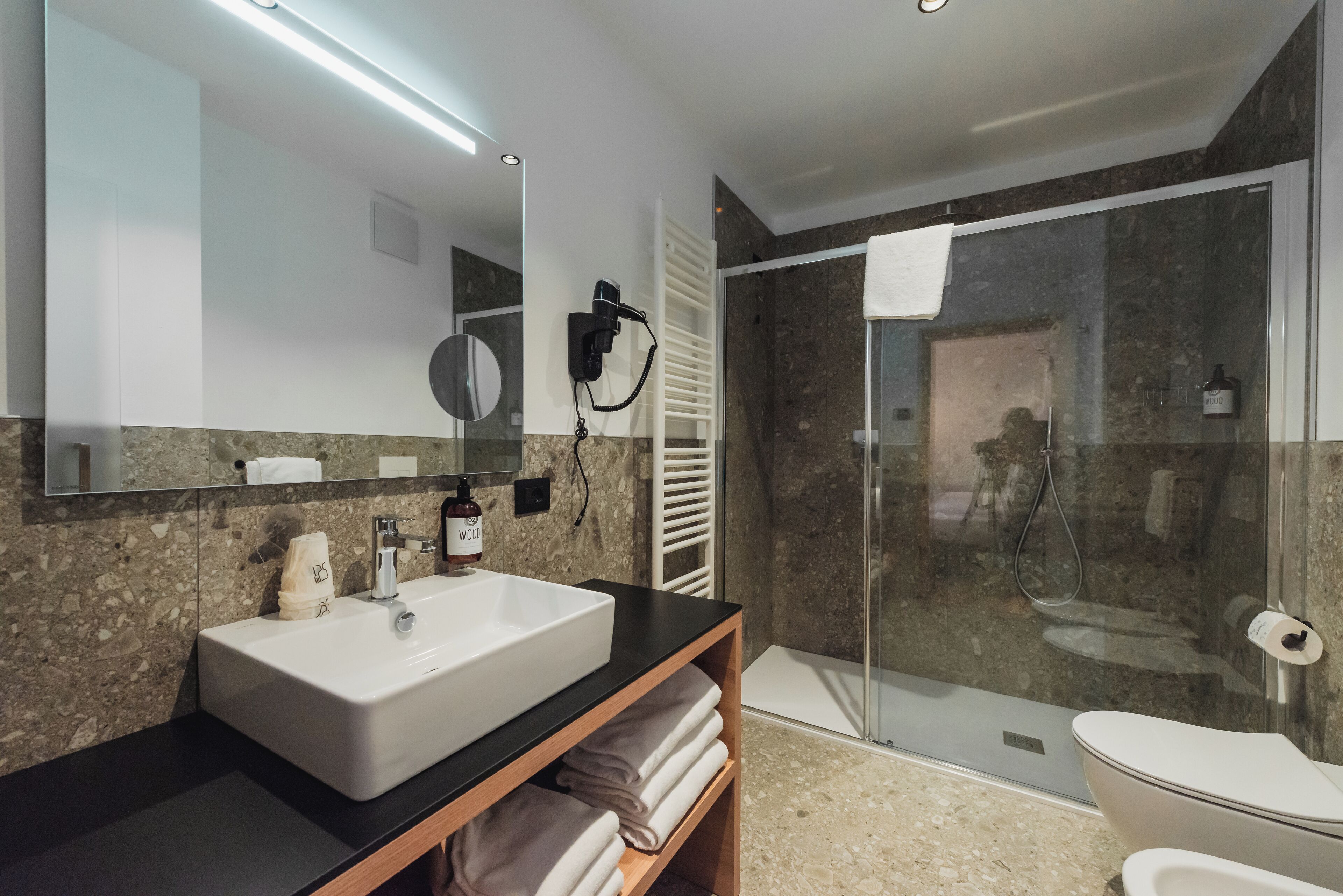 A modern bathroom with a large mirror, a white sink, a glass shower enclosure, and a toilet.