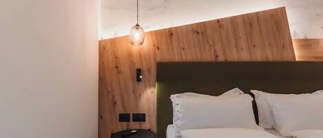 Un dormitorio con cabecera de madera, cama con ropa blanca, una mesita redonda y una lámpara colgante.