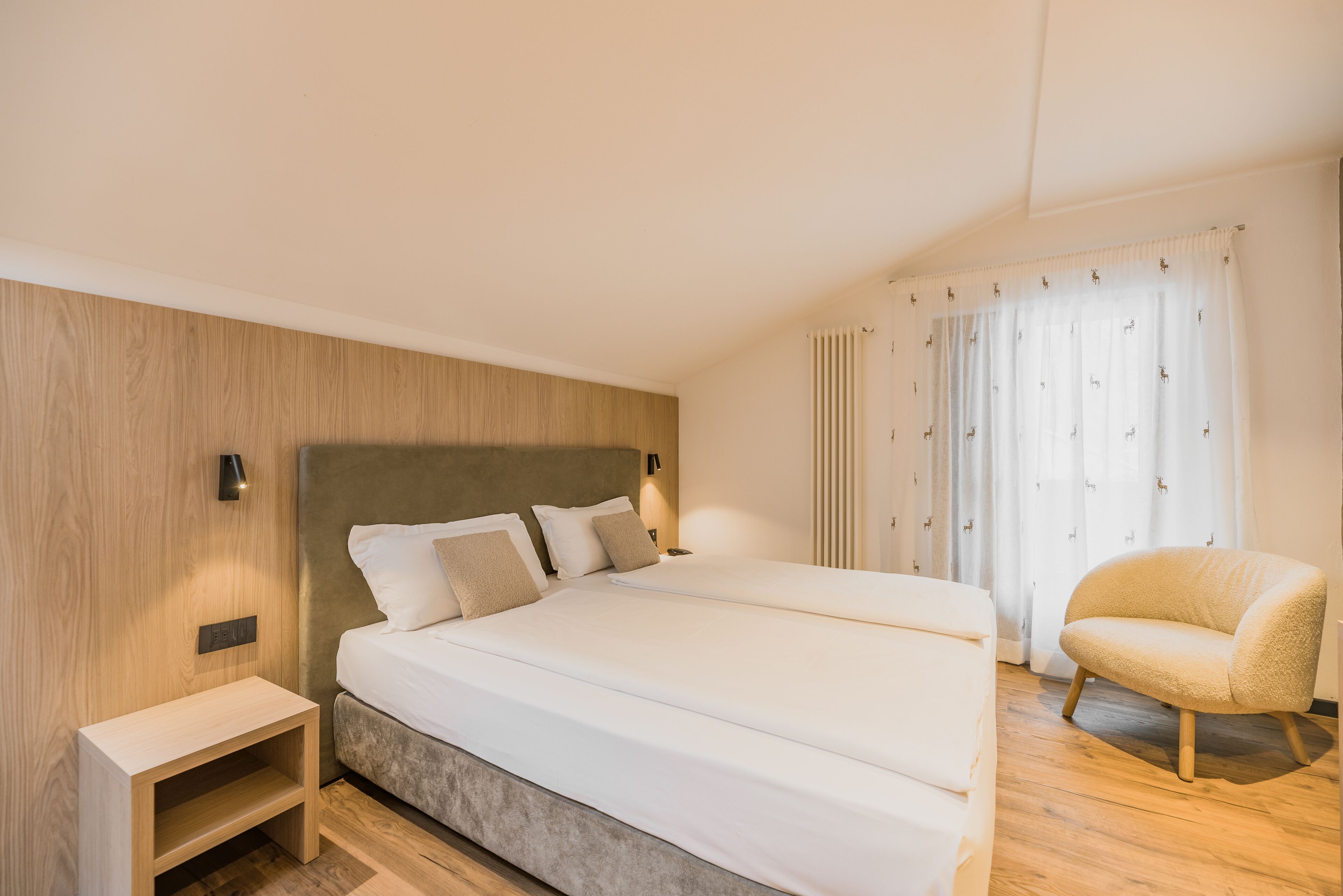 A modern hotel room with a large bed, bedside tables, a chair, and a window with curtains.