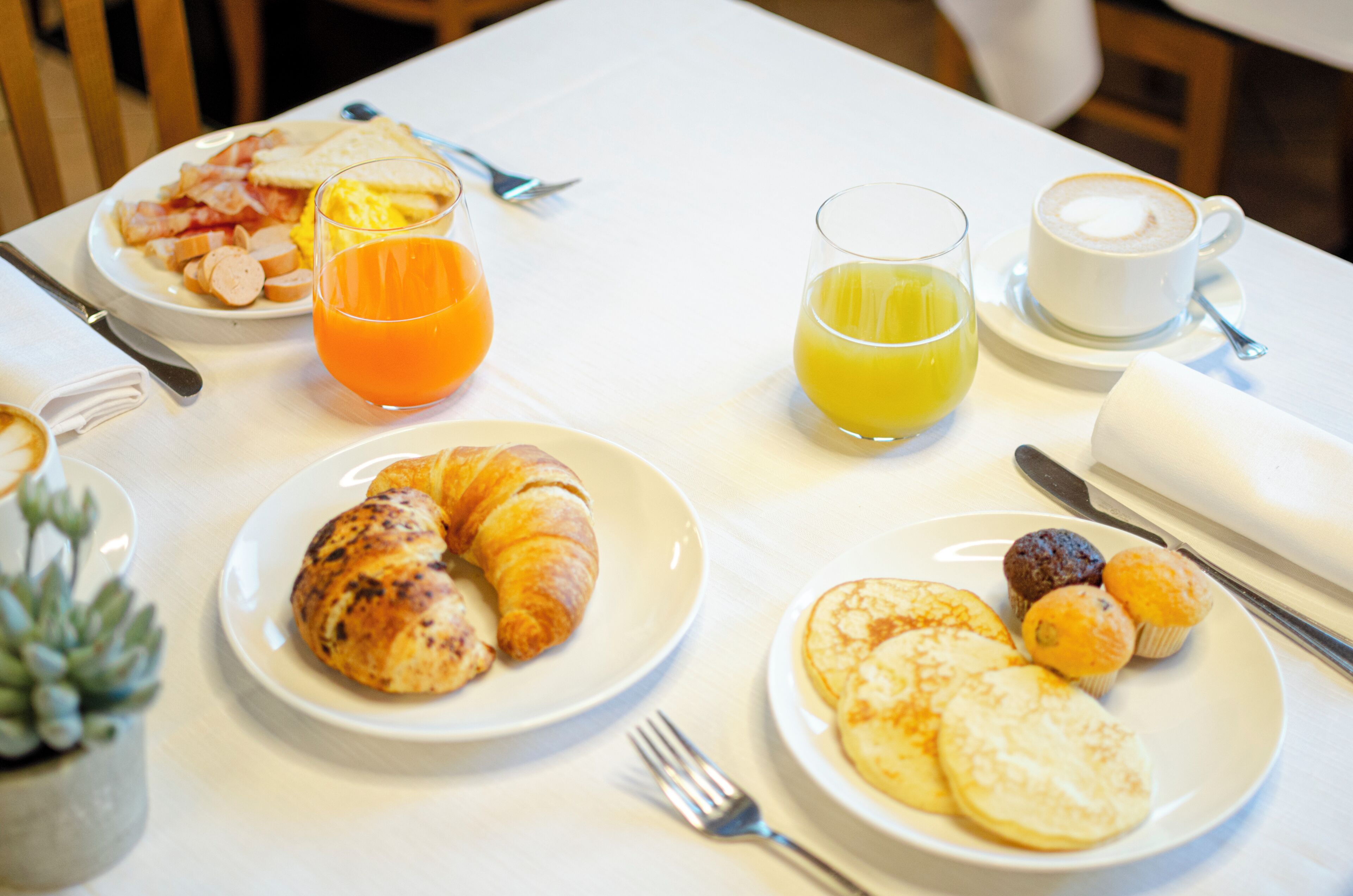 Taula de petit esmorzar amb plats de menjar, gots de suc d'aranja i una tassa de cafè.