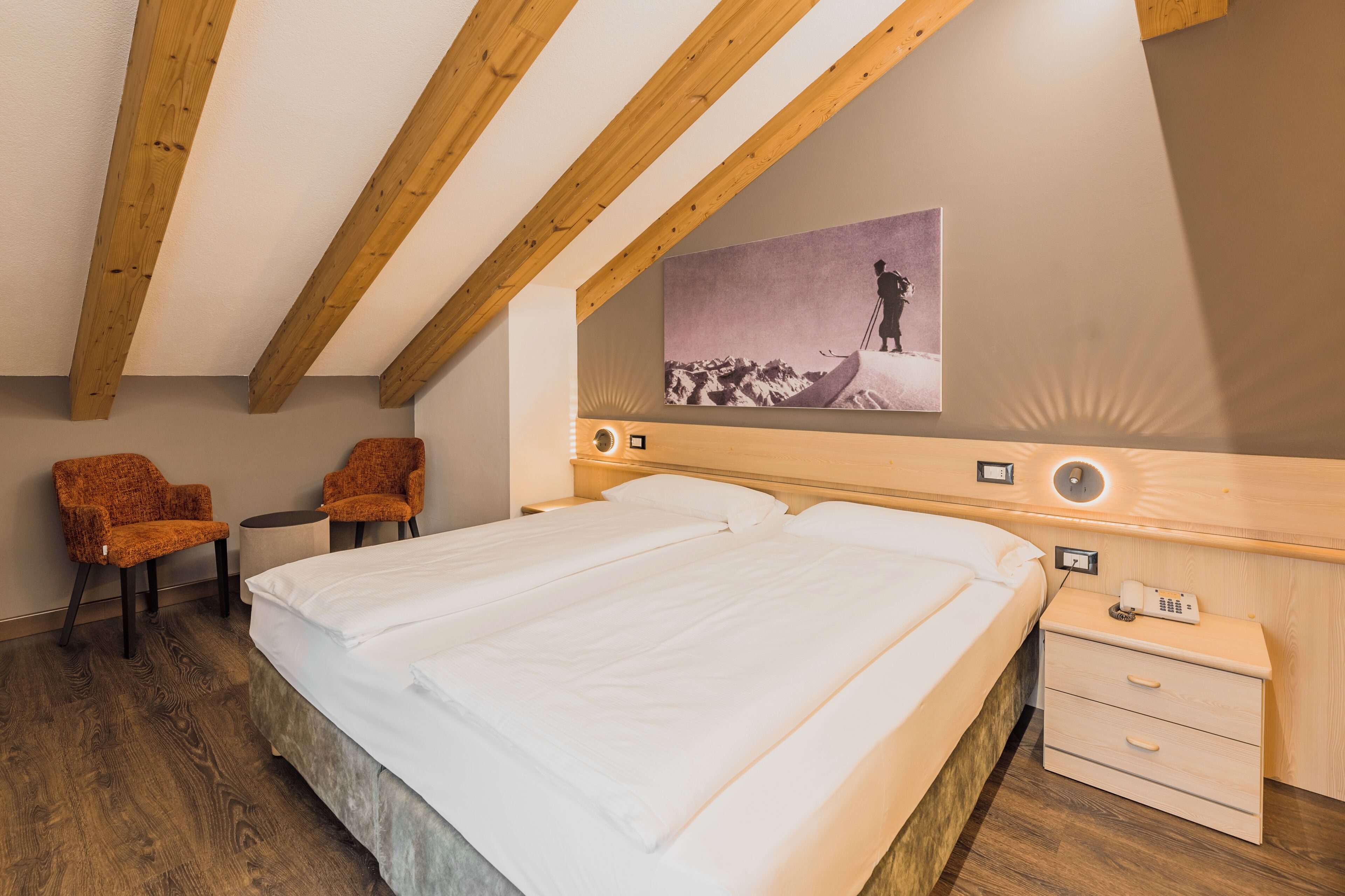 A hotel room with a large bed, two chairs, a bedside table, a nightstand, and a painting on the wall.