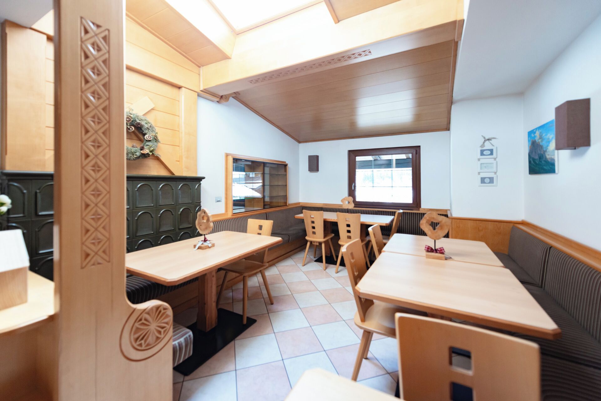 Ein Restaurant mit Holztischen und -sitzen, einem Fliesenboden und Blick ins Freie durch ein Fenster.