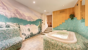 A spa area with a mosaic floor, a hot tub, and a mural of a mountain landscape.