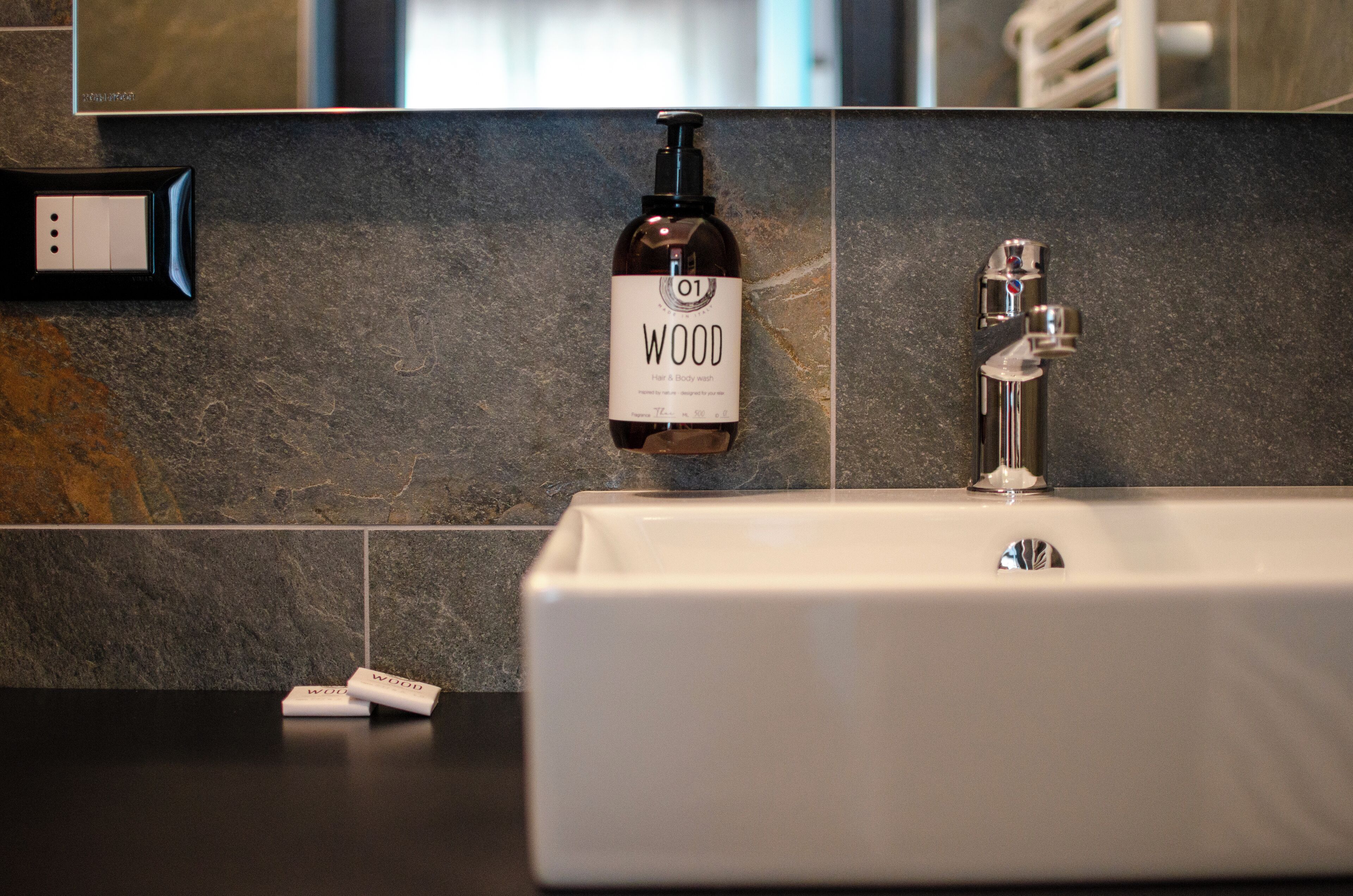 Une salle de bain avec un lavabo blanc, une bouteille de gel douche Wood et un robinet moderne.
