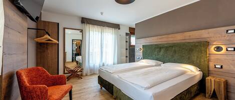 Una habitación de hotel moderna con una cama grande, dos sillones naranjas, un televisor y suelo de madera.