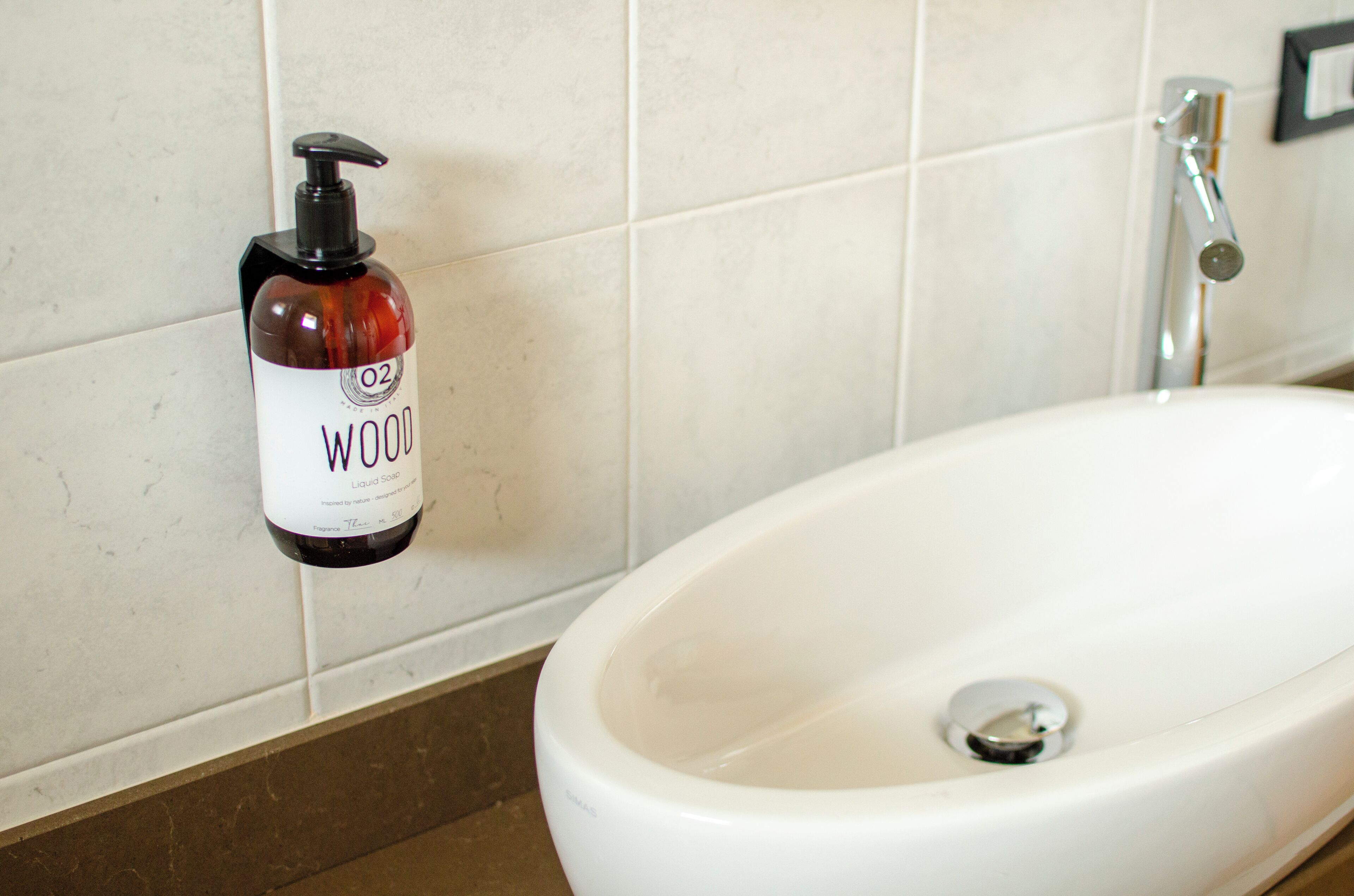 A bathroom with a white sink, a bottle of liquid soap, and a chrome faucet.