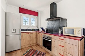 Compact kitchen with a stainless steel refrigerator, oven, and microwave. Features wooden cabinets and a colorful rug.