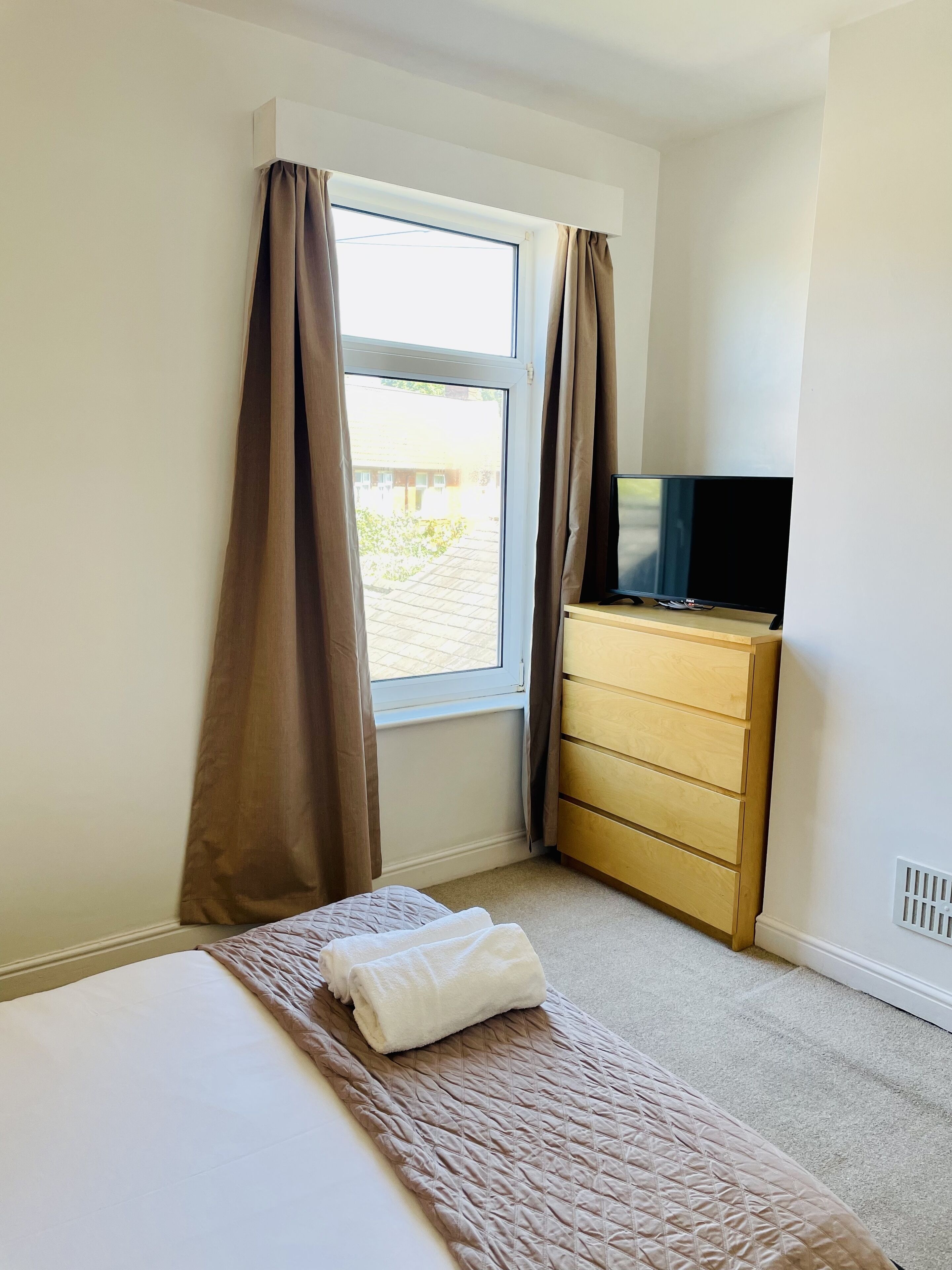 Una habitación de hotel con una cama, un televisor sobre una cómoda de madera y una ventana con cortinas.