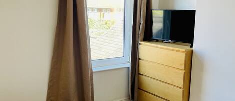 Una habitación de hotel con una cama, un televisor sobre una cómoda de madera y una ventana con cortinas.