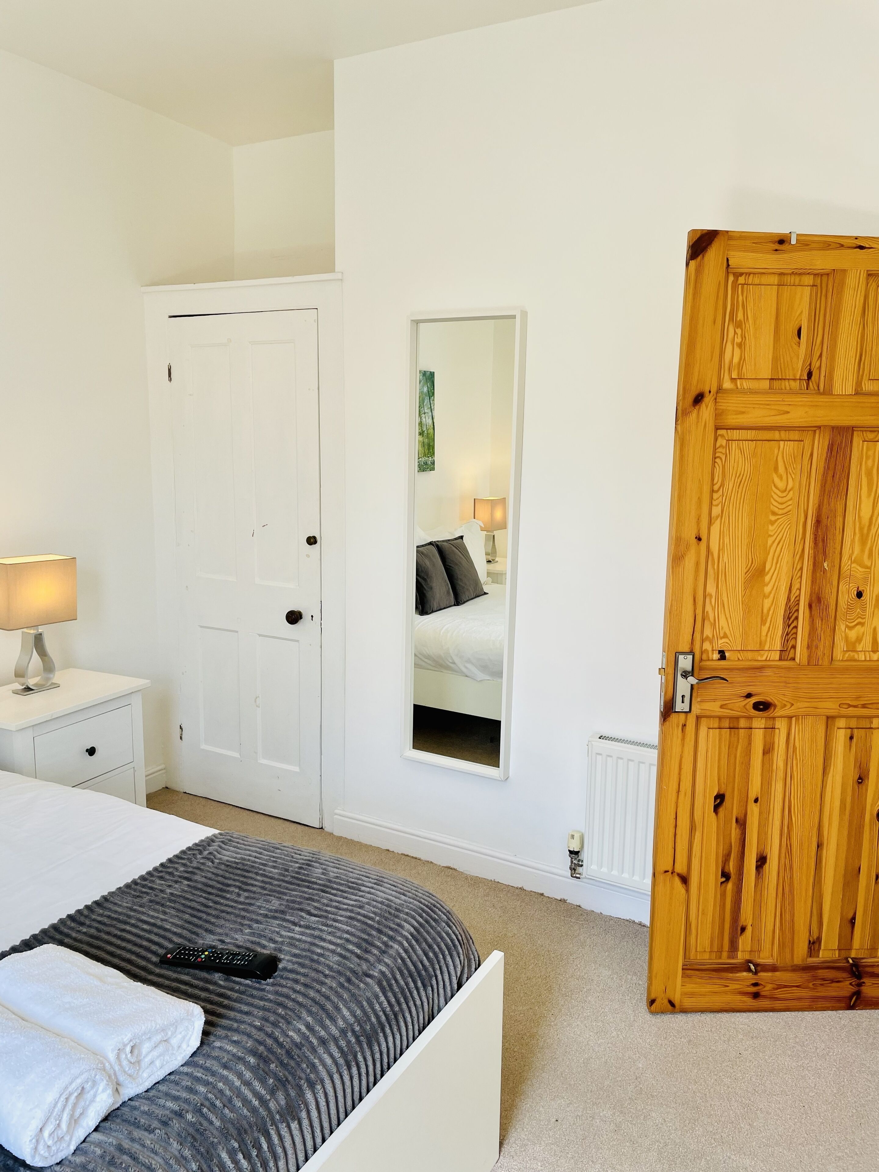 Un dormitorio con cama, mesita de noche, lámpara, puerta de madera y espejo.