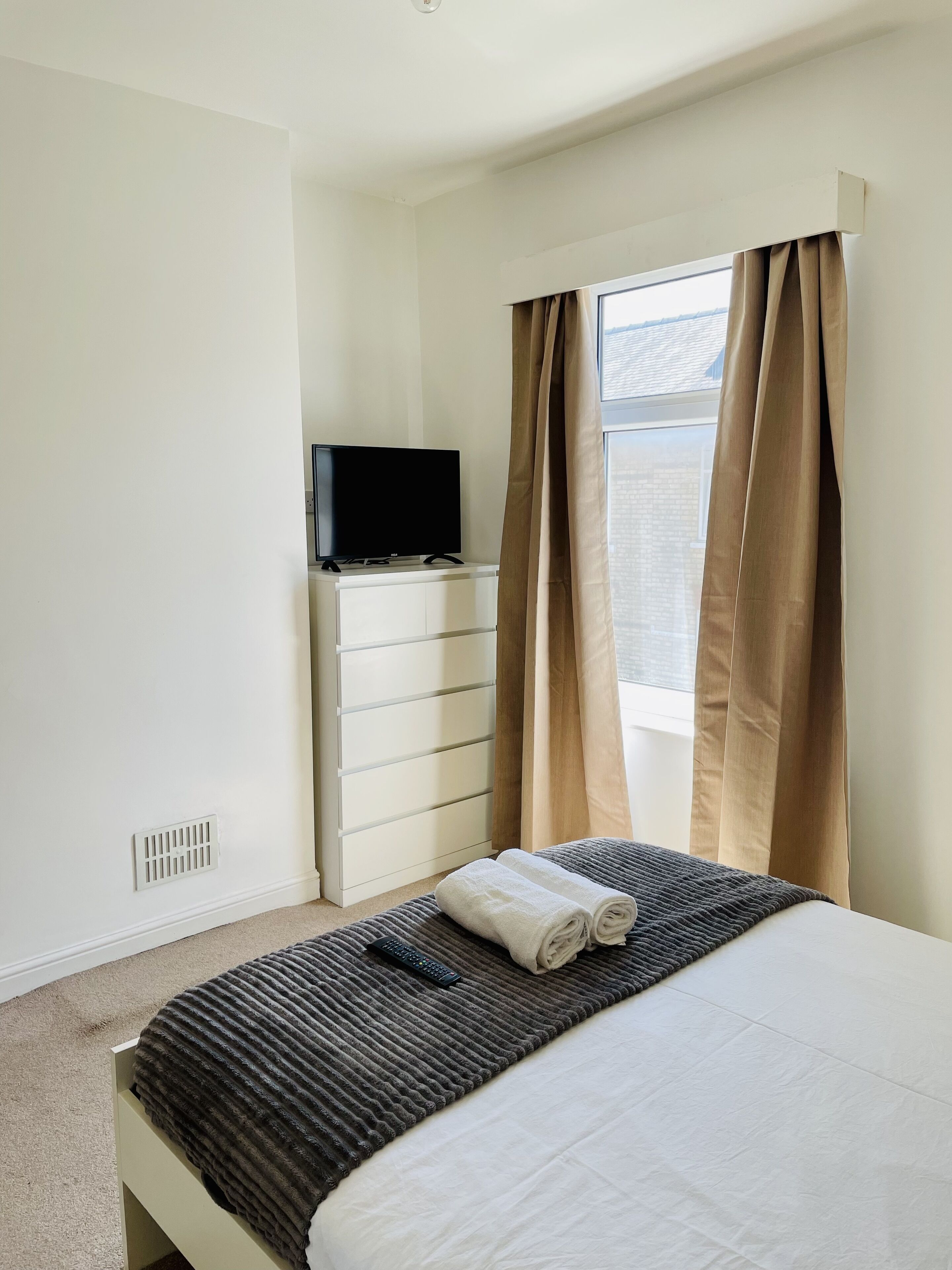 A hotel room with a bed, a TV on a dresser, and a window with curtains.
