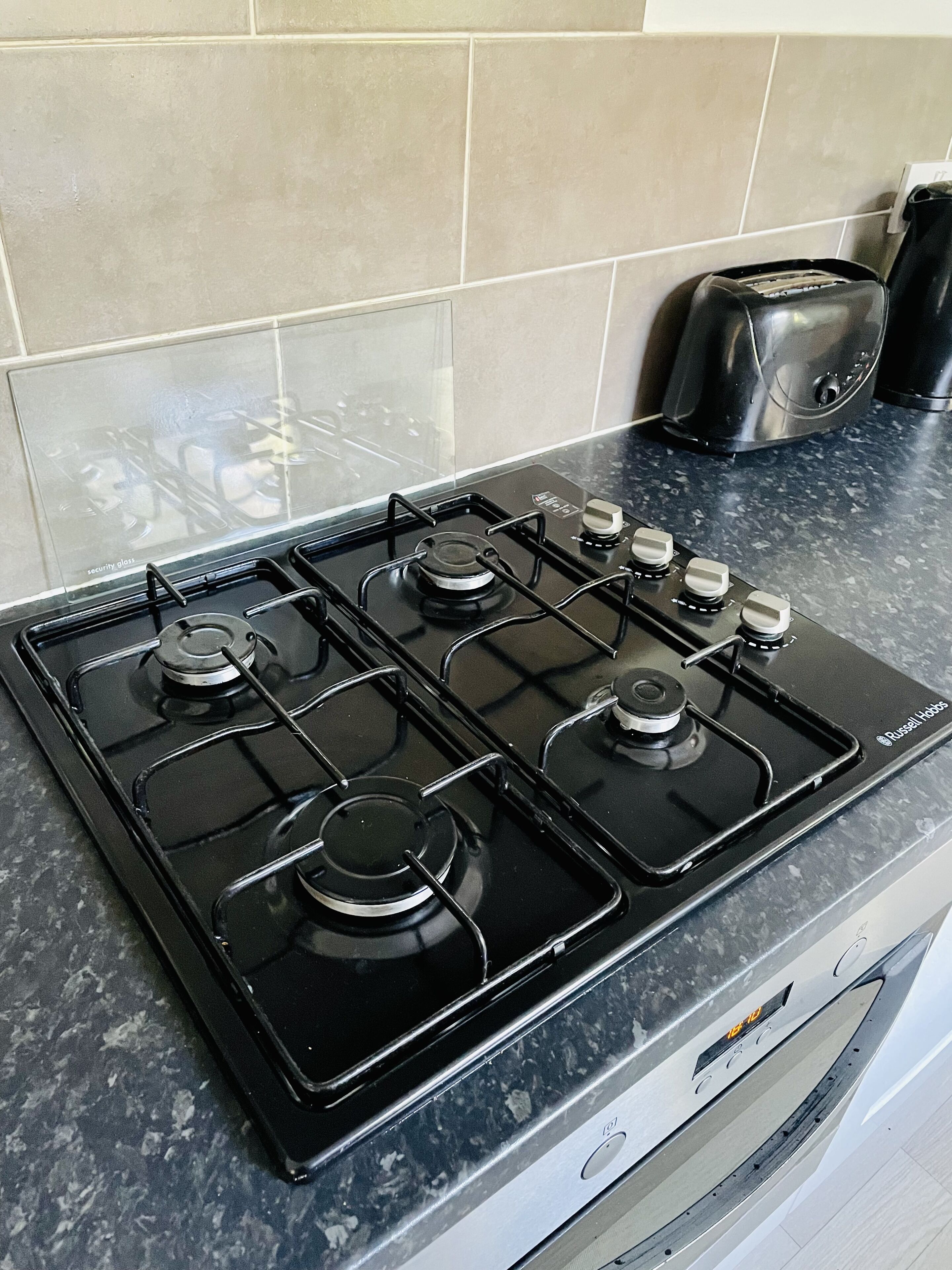 Une cuisine avec un cuisinière à gaz noire, dotée de quatre brûleurs, et un grille-pain posé sur le plan de travail.