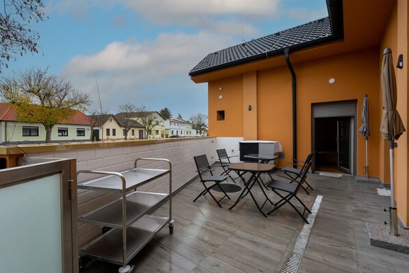 A rooftop patio with a table and chairs, a metal cart, and a sliding glass door leading to an interior space. - Pension Pannonia (Parndorf)