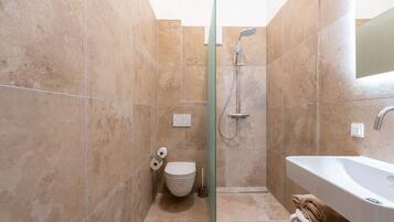 Un baño moderno con cabina de ducha de vidrio, un lavabo blanco y un inodoro.
