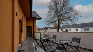 An outdoor patio with a table and chairs, a door, and a tree in the background.