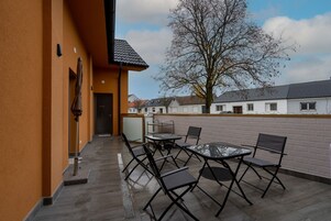 Un patio exterior con una mesa, sillas, una puerta y un árbol al fondo.
