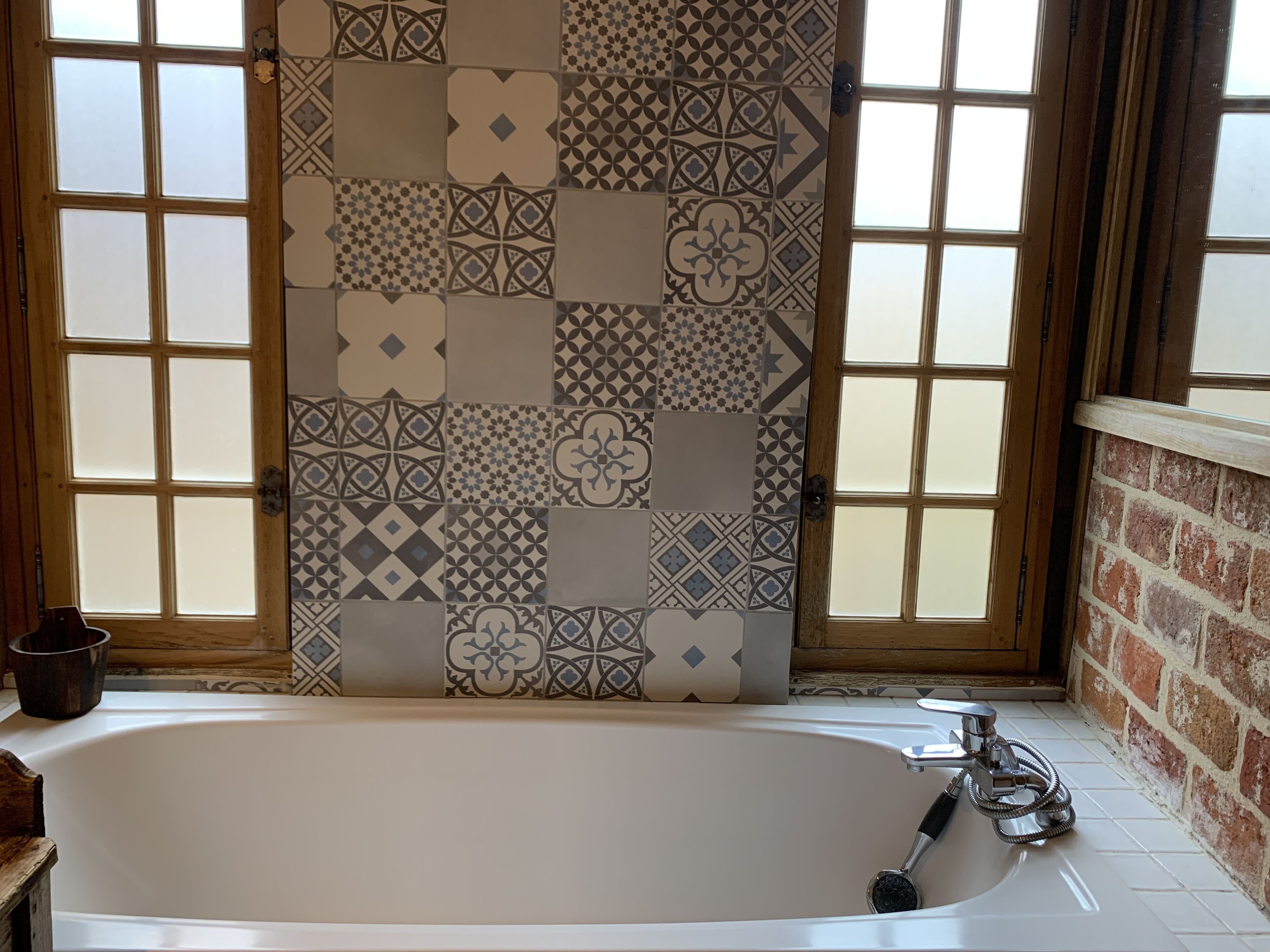 A bathroom with a bathtub, patterned tiles, and a wooden door.