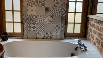 A bathroom with a bathtub, patterned tiles, and a wooden door.