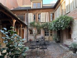 Un patio con un edificio de ladrillo, una pérgola de madera y una mesa con sillas.