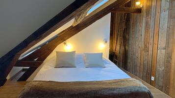 A cozy attic bedroom with a sloped ceiling, wooden beams, and a bed with white linens.