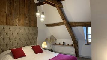 A bedroom with a wooden ceiling, a tufted headboard, two red pillows, a white bedspread, and a purple blanket.