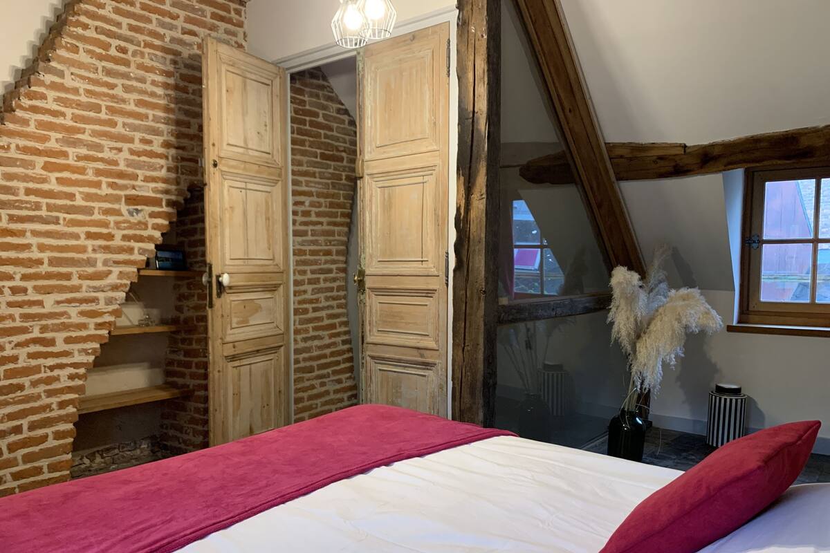 Un dormitorio con pared de ladrillo, armario de madera y cama con almohadas rojas.