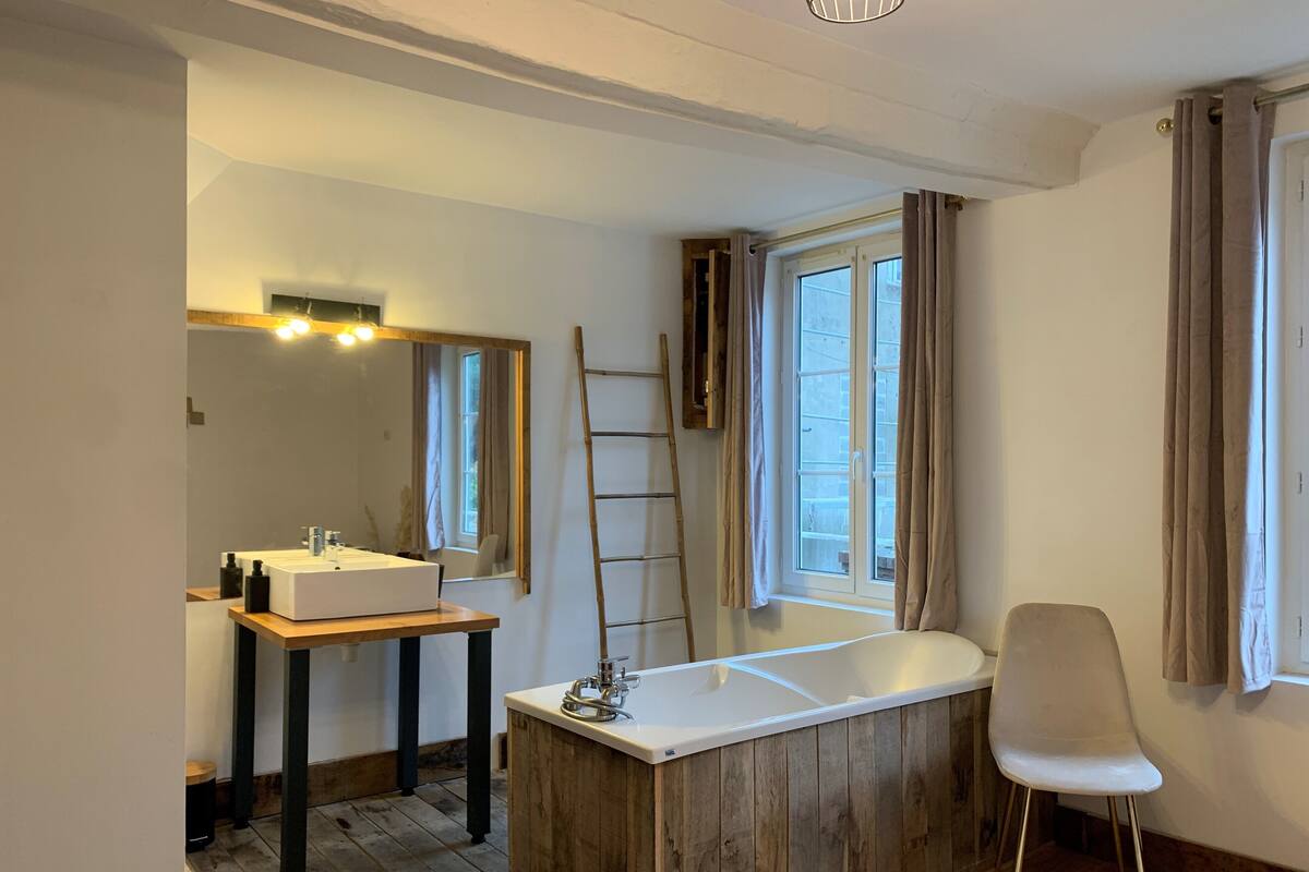 Un baño moderno con tocador de madera, una bañera grande, un espejo y una ventana con cortinas.