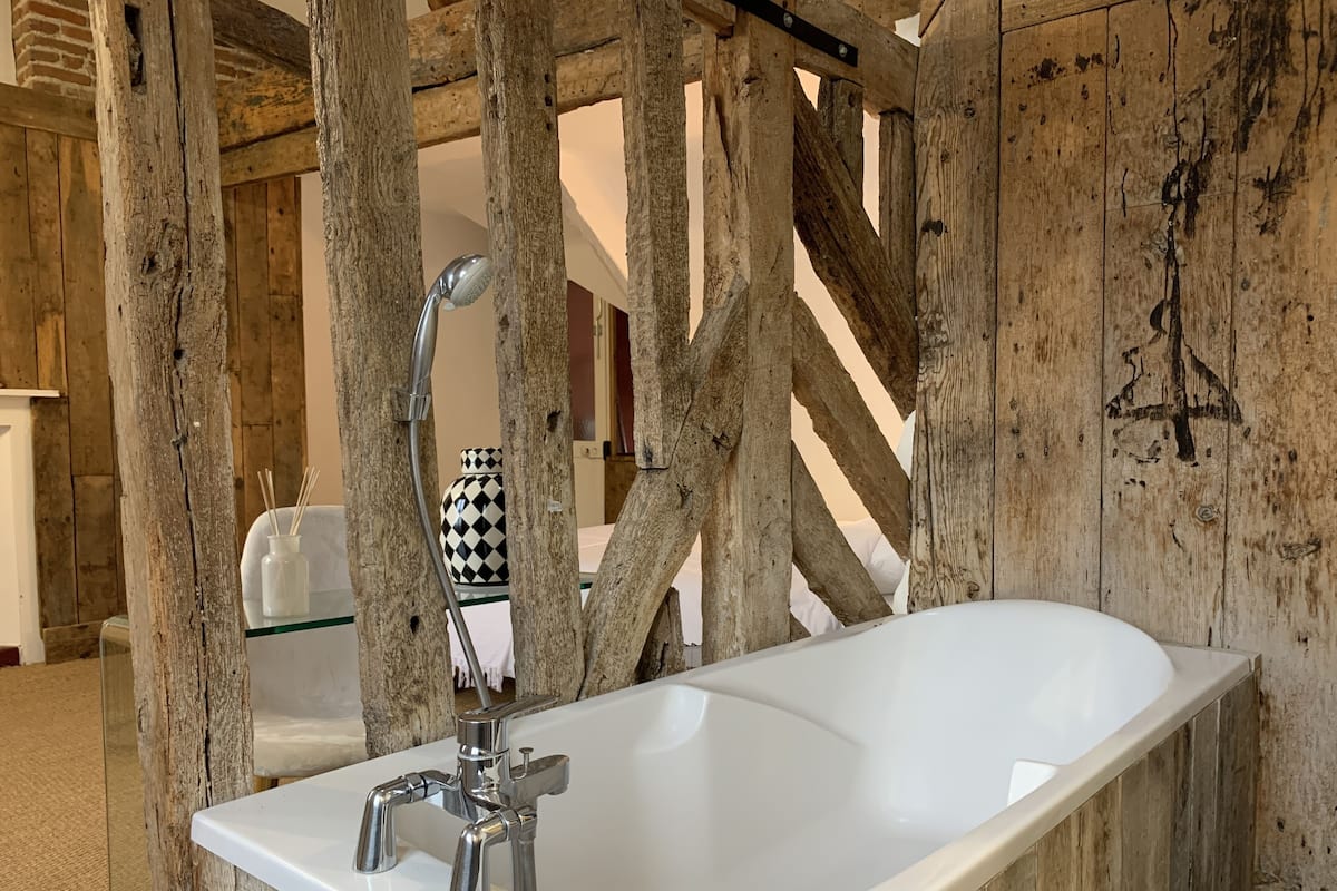 Un baño con una bañera blanca, vigas de madera y un florero a cuadros en el mostrador.