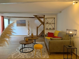 Una sala de estar acogedora con un sofá, una mesita redonda, una lámpara y una escalera.