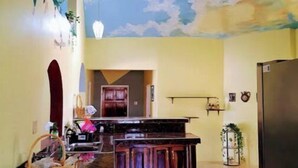 Une cuisine dotée d’un îlot central, d’un coin repas avec un plafond haut et une fresque murale, ainsi que d’un réfrigérateur.