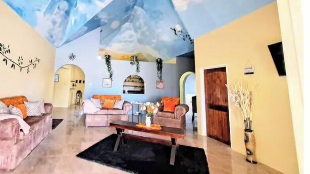 Un vaste salon doté d’un plafond haut peint pour évoquer un ciel nuageux, deux canapés, une table basse et un vase décoratif.