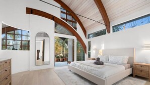 Un dormitorio moderno con una cama grande, vigas de madera en el techo y ventanas amplias.