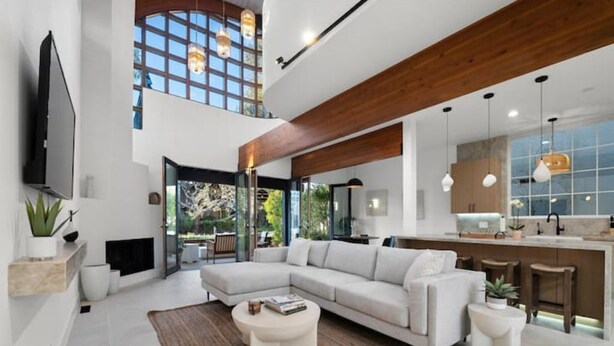 Amplia sala de estar con un sofá modular grande, una mesa de centro y un televisor montado en la pared. Cuenta con una zona de cocina con barra y iluminación colgante.