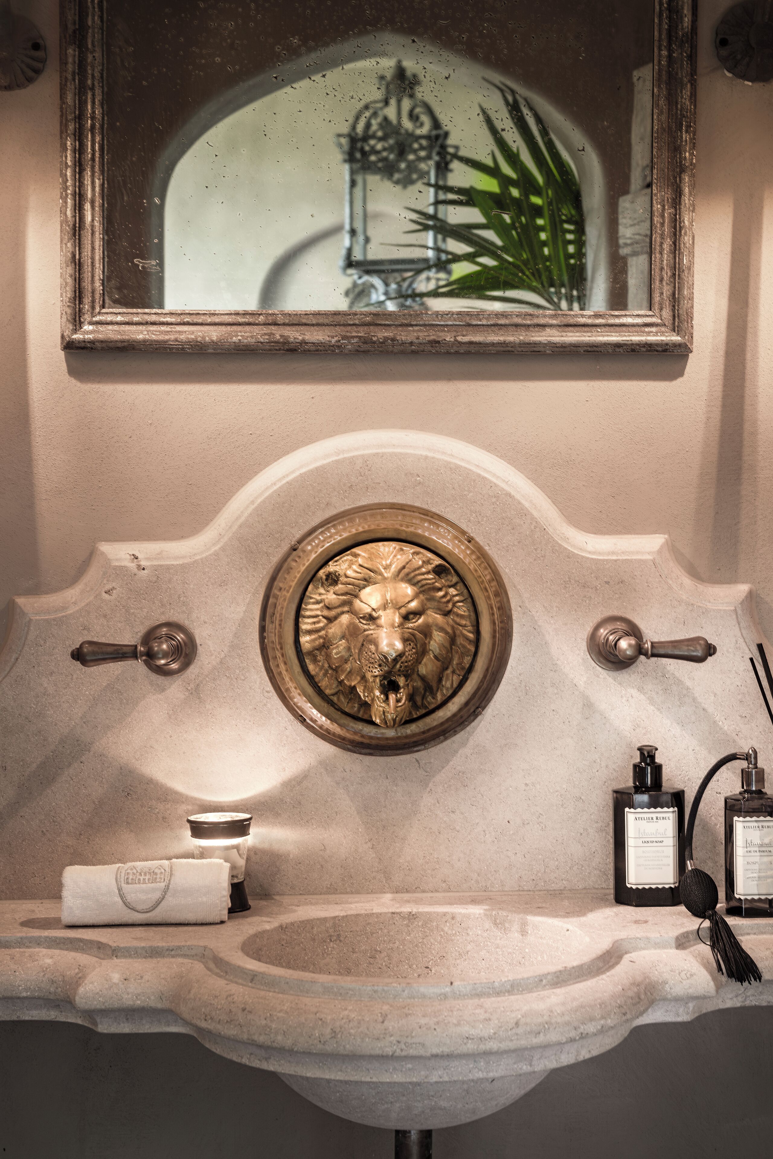 A bathroom with a stone sink, a mirror, and a decorative lion head.