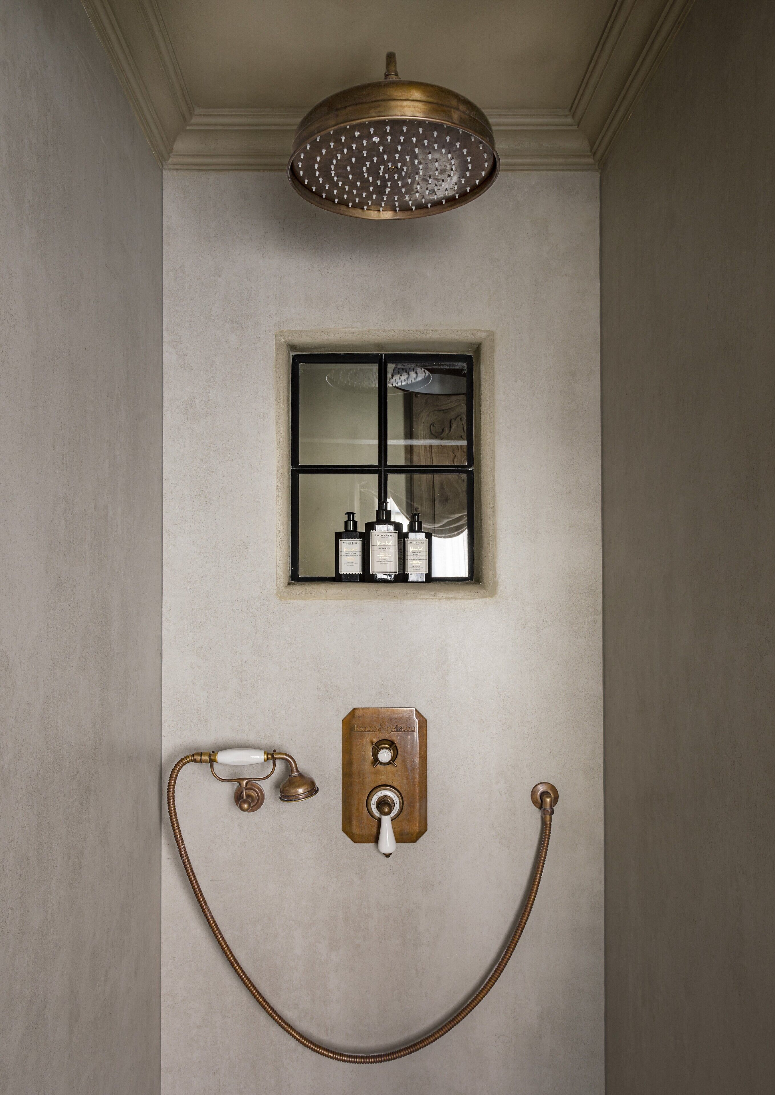 A bathroom with a shower, a window with bottles, and a light fixture.