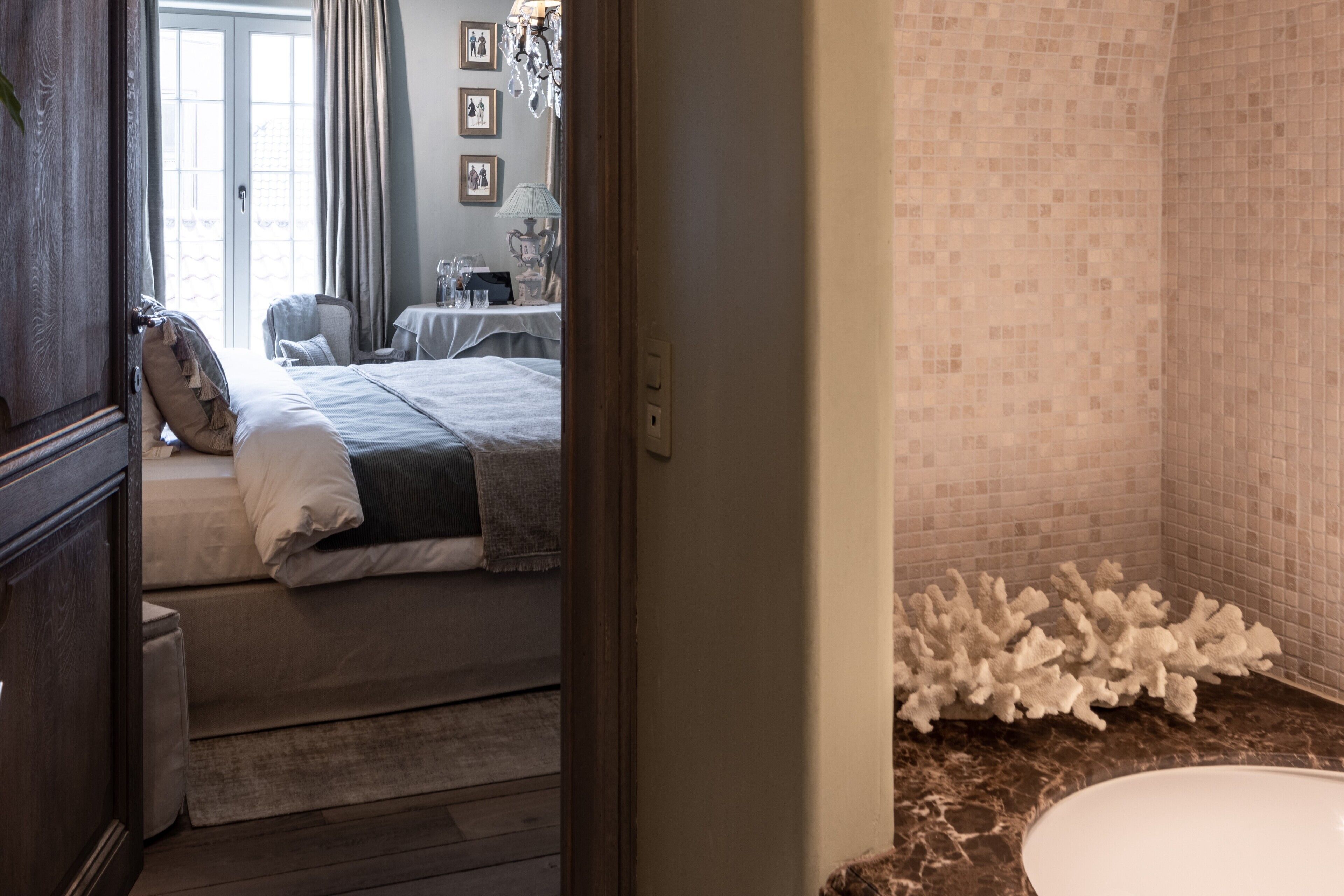 A bedroom with a bed, bedside table, and a view of a bathroom with a sink and tiled walls.