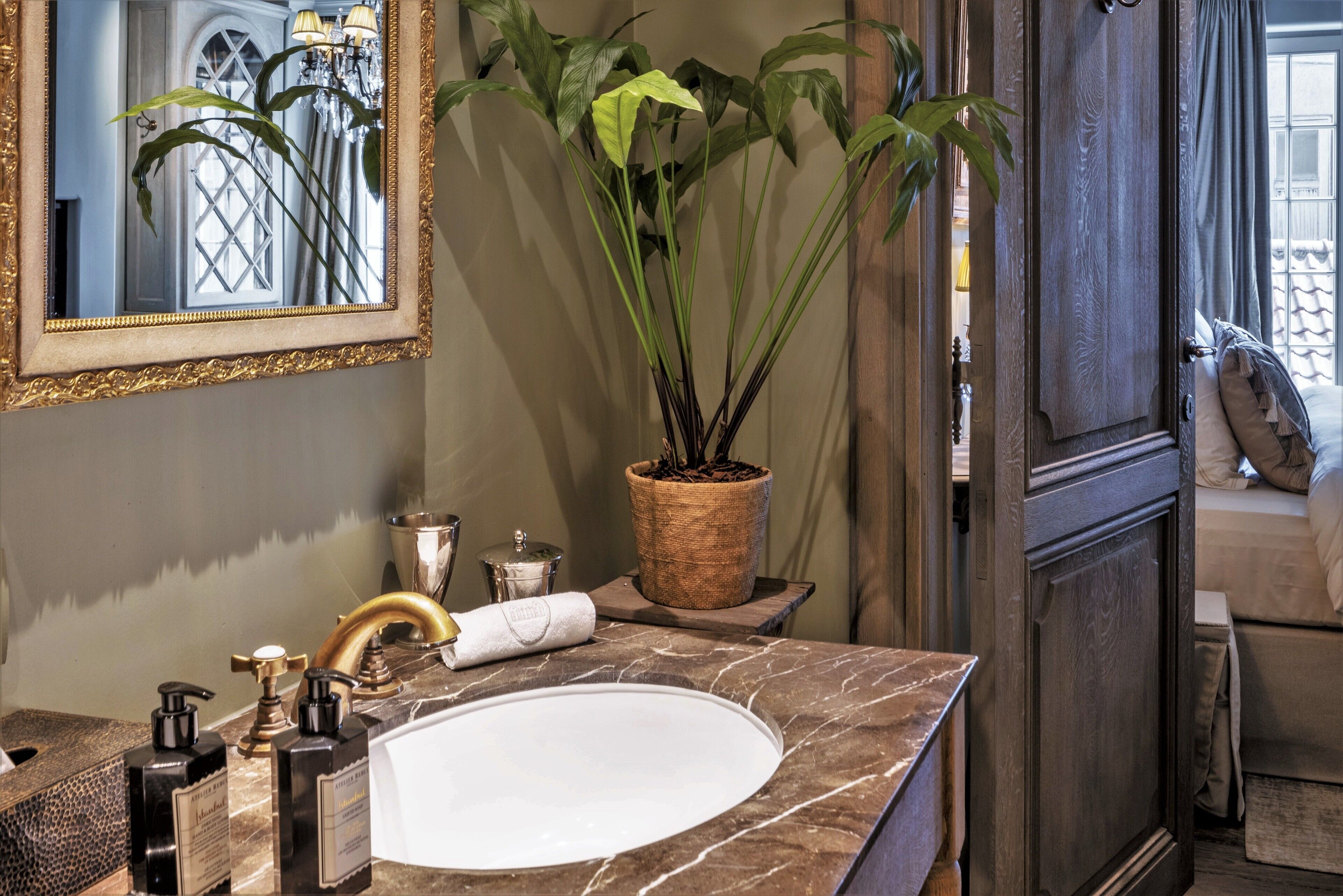 A bathroom with a marble sink, gold faucets, a large mirror, and a potted plant.
