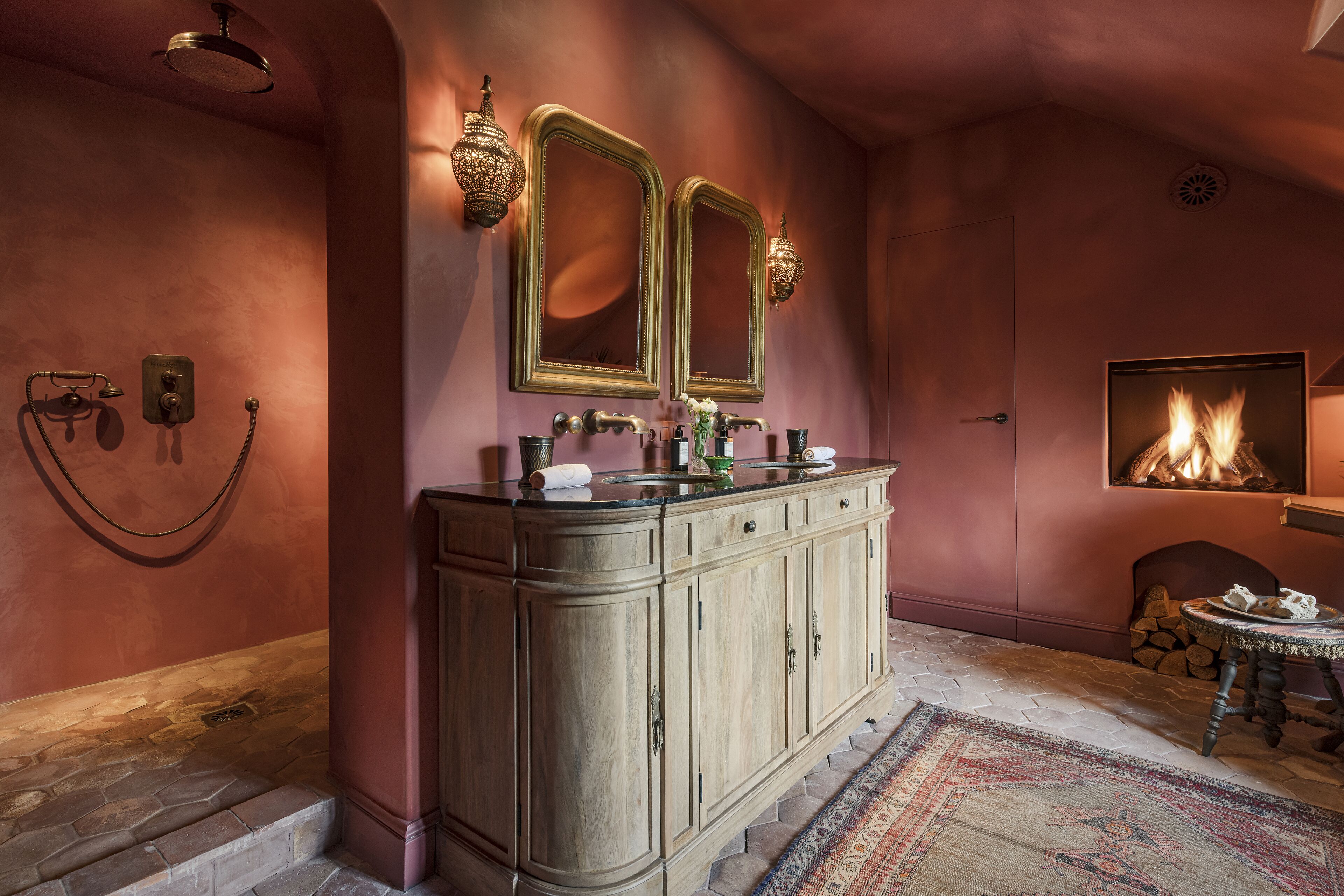 Een badkamer met een houten wastafelmeubel, twee spiegels, een wastafel en een open haard.