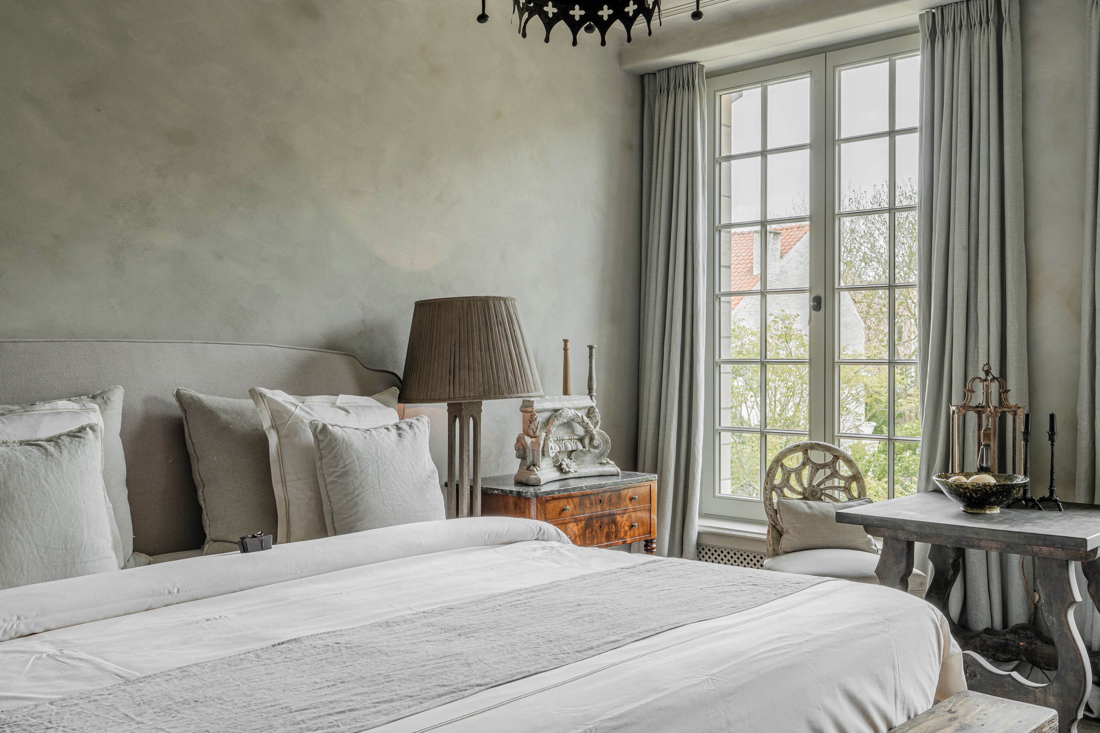 A bedroom with a large bed, a nightstand, a lamp, and a window with curtains.