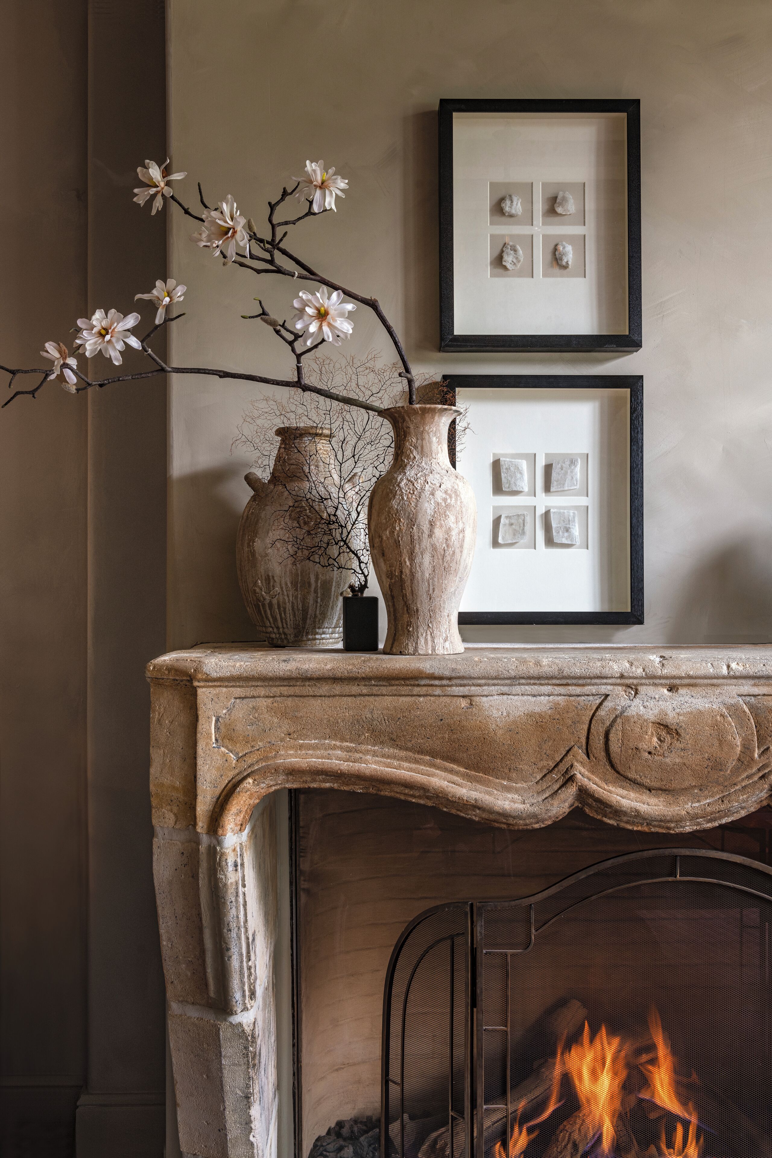 A fireplace mantel with two vases and a branch of white flowers.