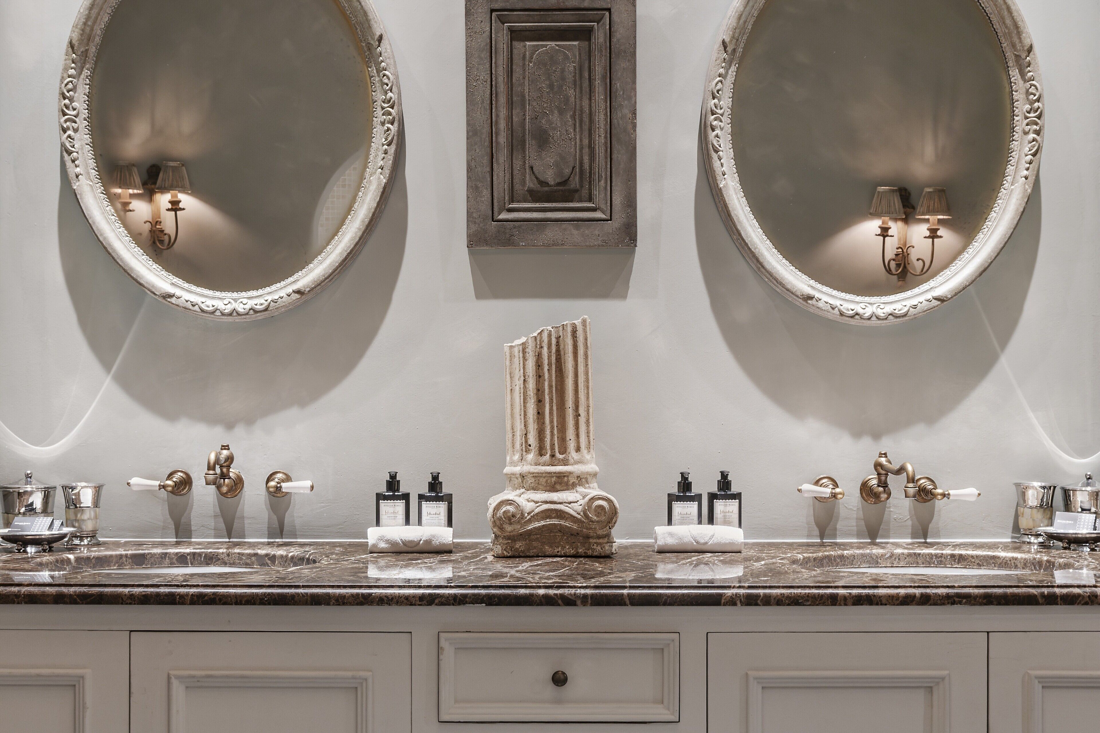 A bathroom with two large oval mirrors, a marble countertop, and a central decorative column.