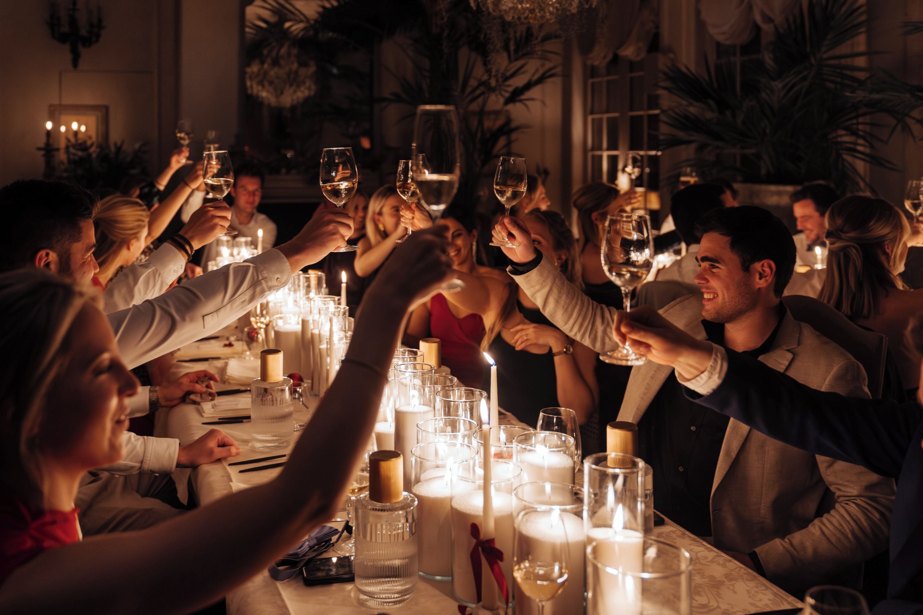 A group of people toasting at a dinner table with candles and glasses of wine.