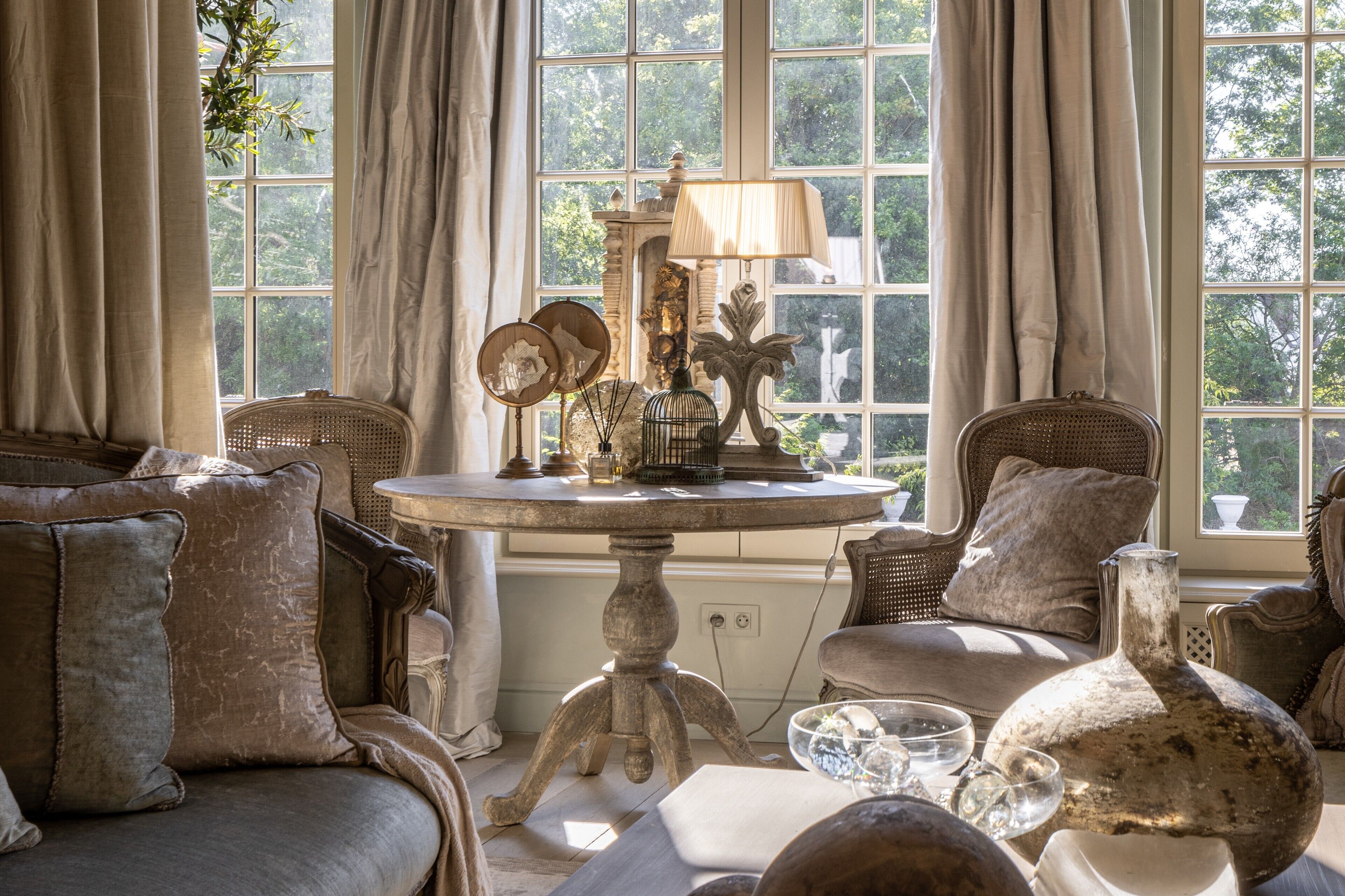 A room with a round table, wicker chairs, and a large window with curtains.