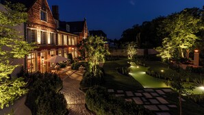A well-lit courtyard with a paved pathway, neatly trimmed hedges, and a small water feature. - The Notary (Bruges)