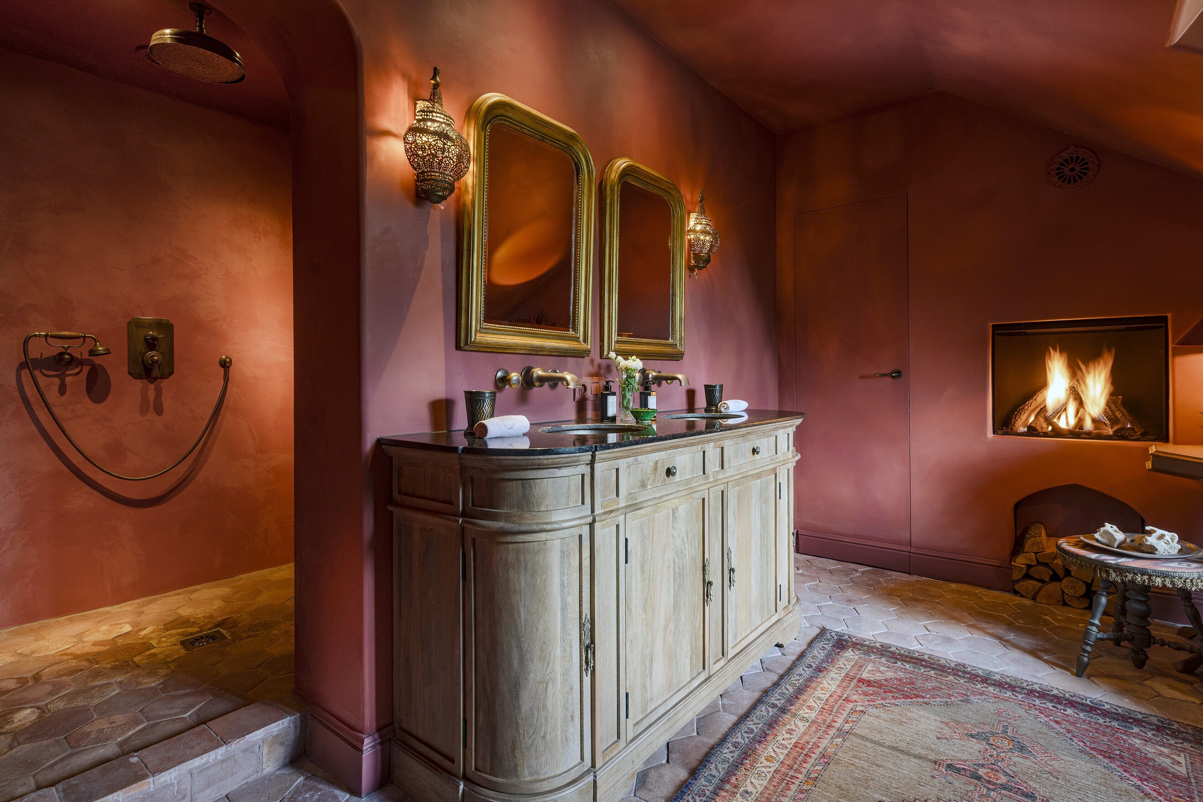 Une salle de bain avec un meuble-lavabo en bois, deux miroirs fixés au mur, un espace douche et une cheminée.