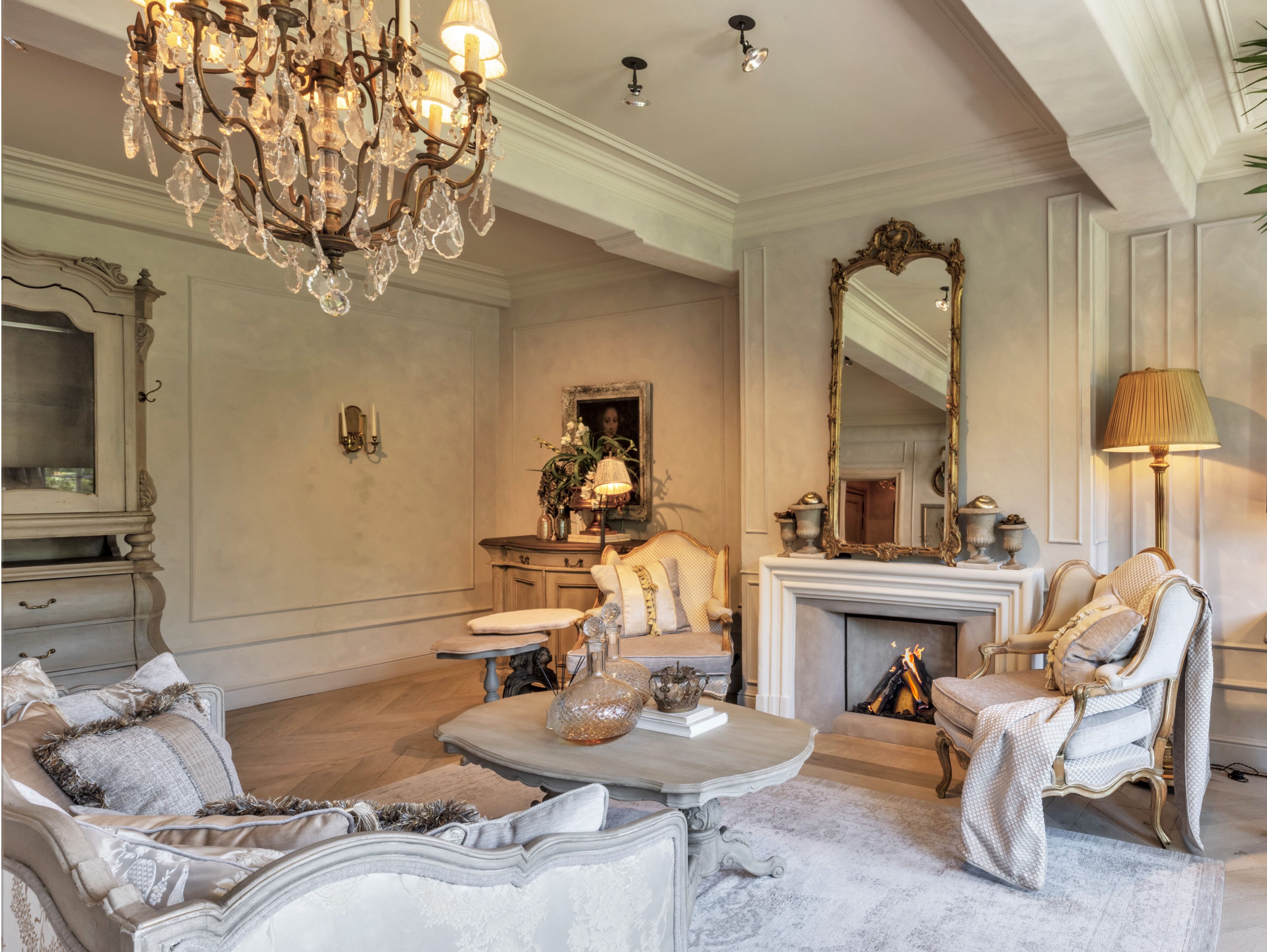 Een luxueuze woonkamer met sierlijk meubilair, een weelderige kroonluchter en een open haard.