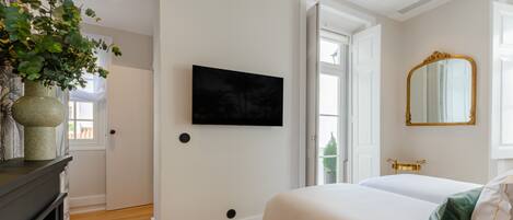 Un dormitorio con una cama, un televisor montado en la pared, un espejo y una puerta que da a otra habitación.